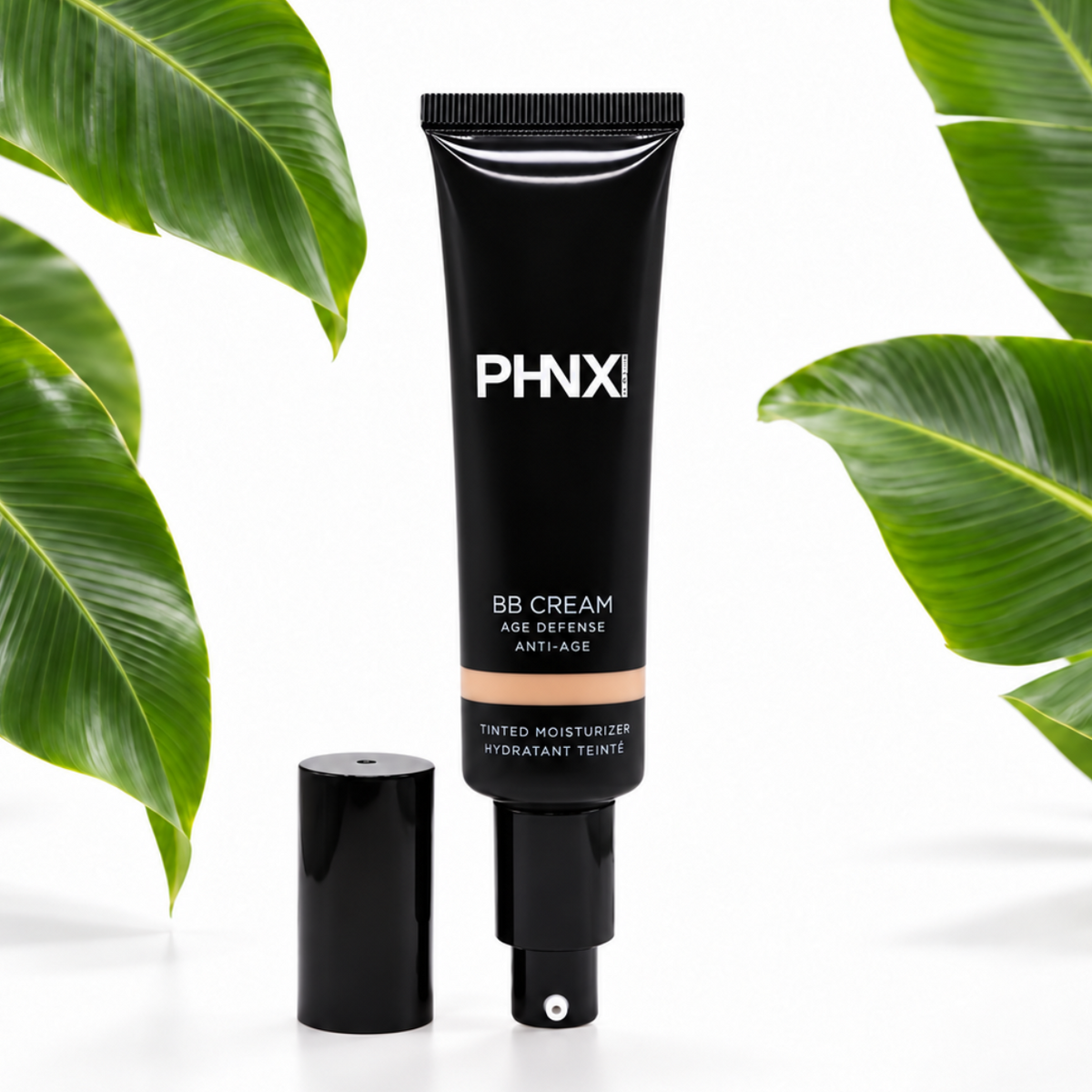 PHNX BB Cream in a black squeeze tube with its cap removed, set against a white background with decorative green tropical leaves on both sides.